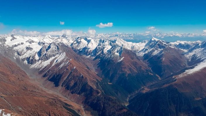 Flugaufnahme: Hohe Berge, hohe Wolkenbasis und im Hintergrund noch viel höhere Berge in kristallklarer Luft.
