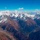 Flugaufnahme: Hohe Berge, hohe Wolkenbasis und im Hintergrund noch viel höhere Berge in kristallklarer Luft.