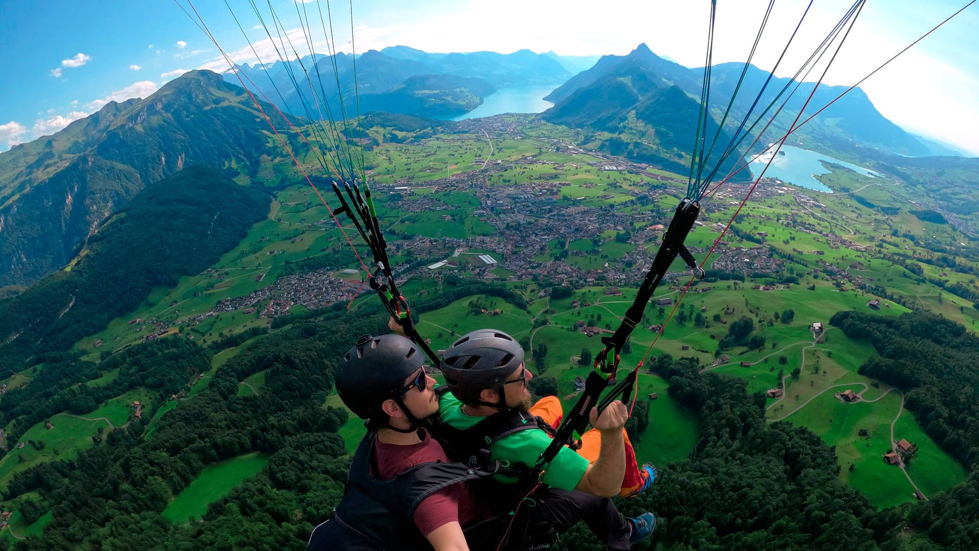 Flugaufnahme: Bei einem Tandemflug von der Rotenflueh übergibt der Pilot die Bremsleinen dem Passagier. Im Hintergrund der Schwyzer Talkessel, der Lauerzersee und ein Teil vom Vierwaldstättersee.