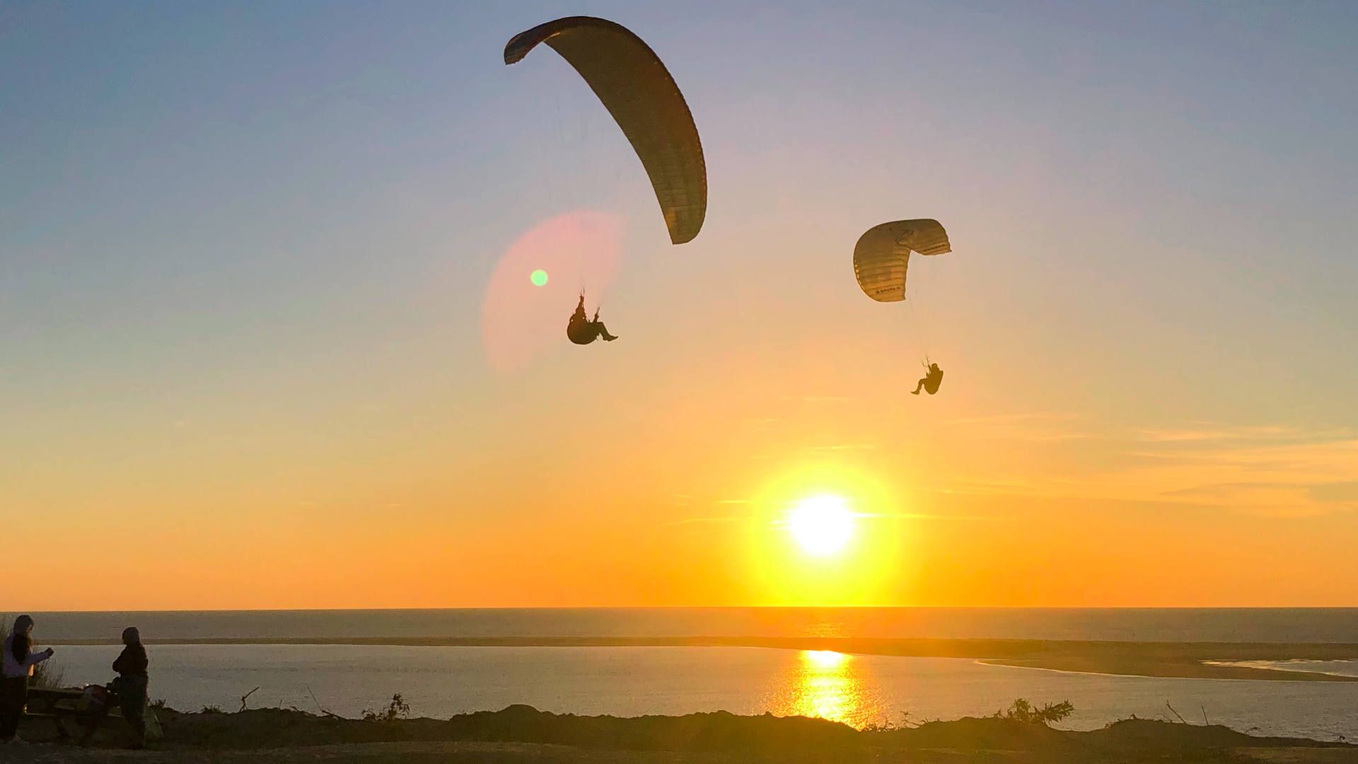 Zwei Gleitschirme tanzen bei Sonnenuntergang um die Wette vor dem Petit Nice Startplatz an der Dune du Pyla.