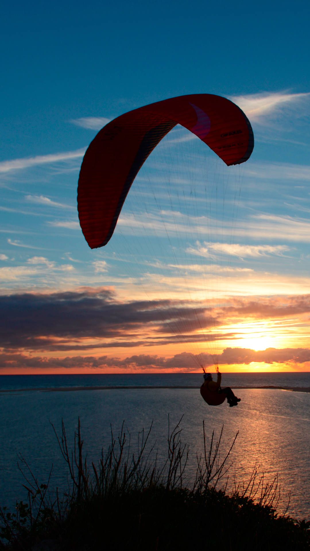 Ein Gleitschirm soart bei Sonnenuntergang mit Blick aufs Meer im laminaren Wind.