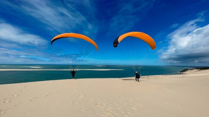 Zwei Gleitschirmpiloten haben ihre Schirme aufgezogen und warten auf stärkeren Wind, damit sie im dynamisch entstehenden Aufwind oben bleiben können.