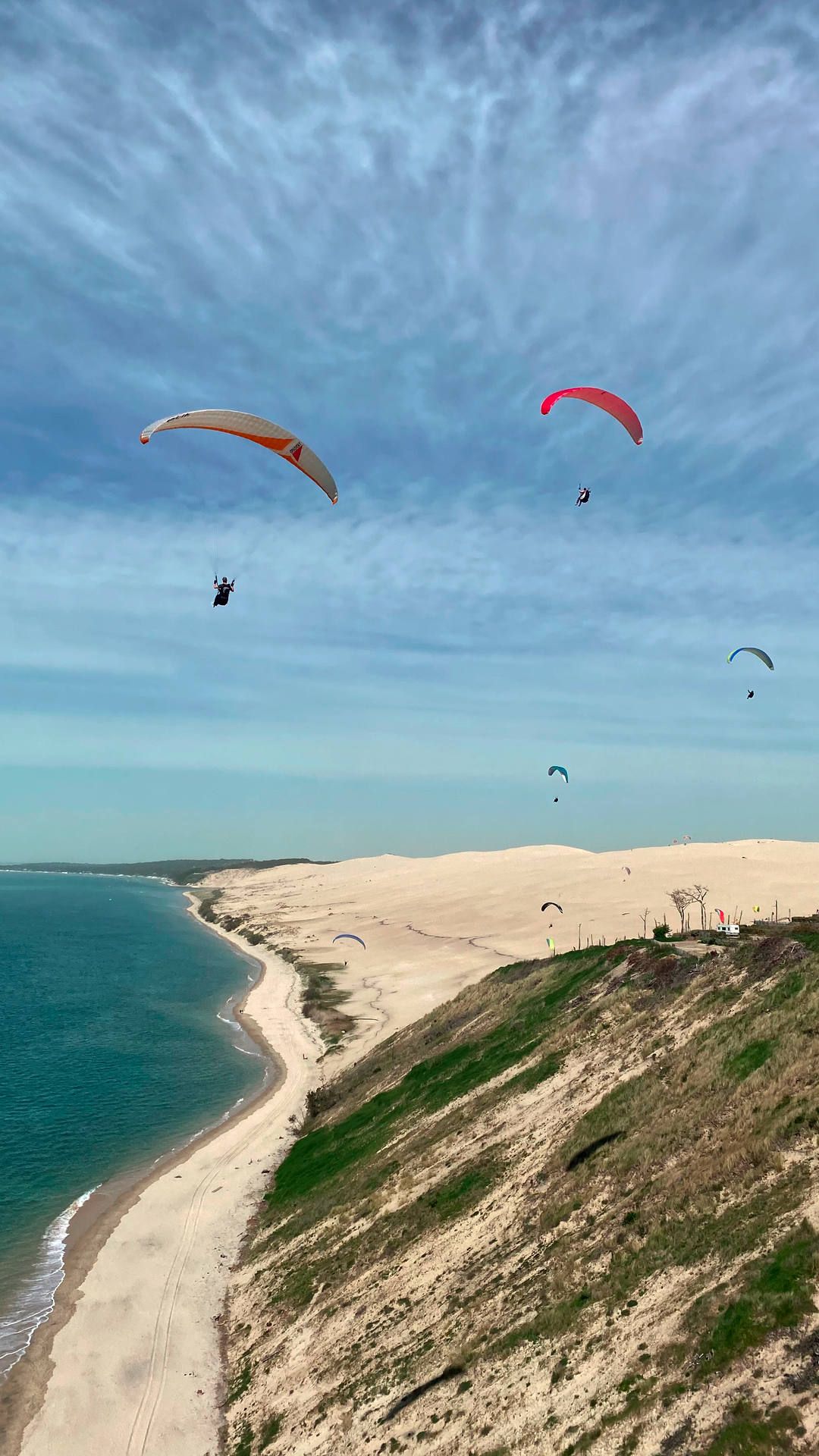 Luftaufnahme: Vier Gleitschirmpiloten fliegen mit ihren Fluggeräten Richtung Norden entlang der grossen Dune du Pyla.