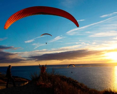 Abendliches Soaring für drei Gleitschirmpiloten an der Dune du Pyla kurz vor Sonnenuntergang.