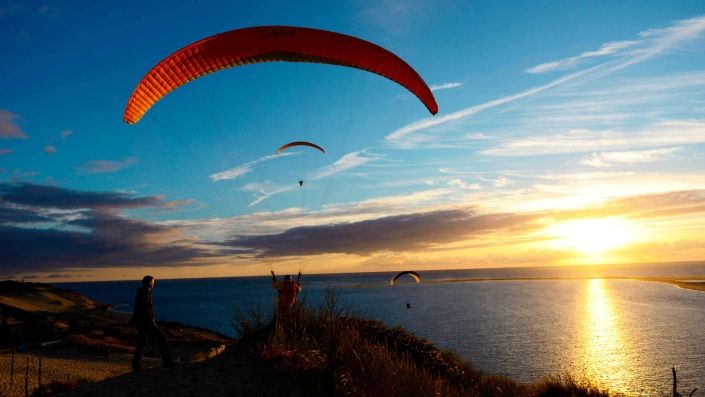 Abendliches Soaring für drei Gleitschirmpiloten an der Dune du Pyla kurz vor Sonnenuntergang.