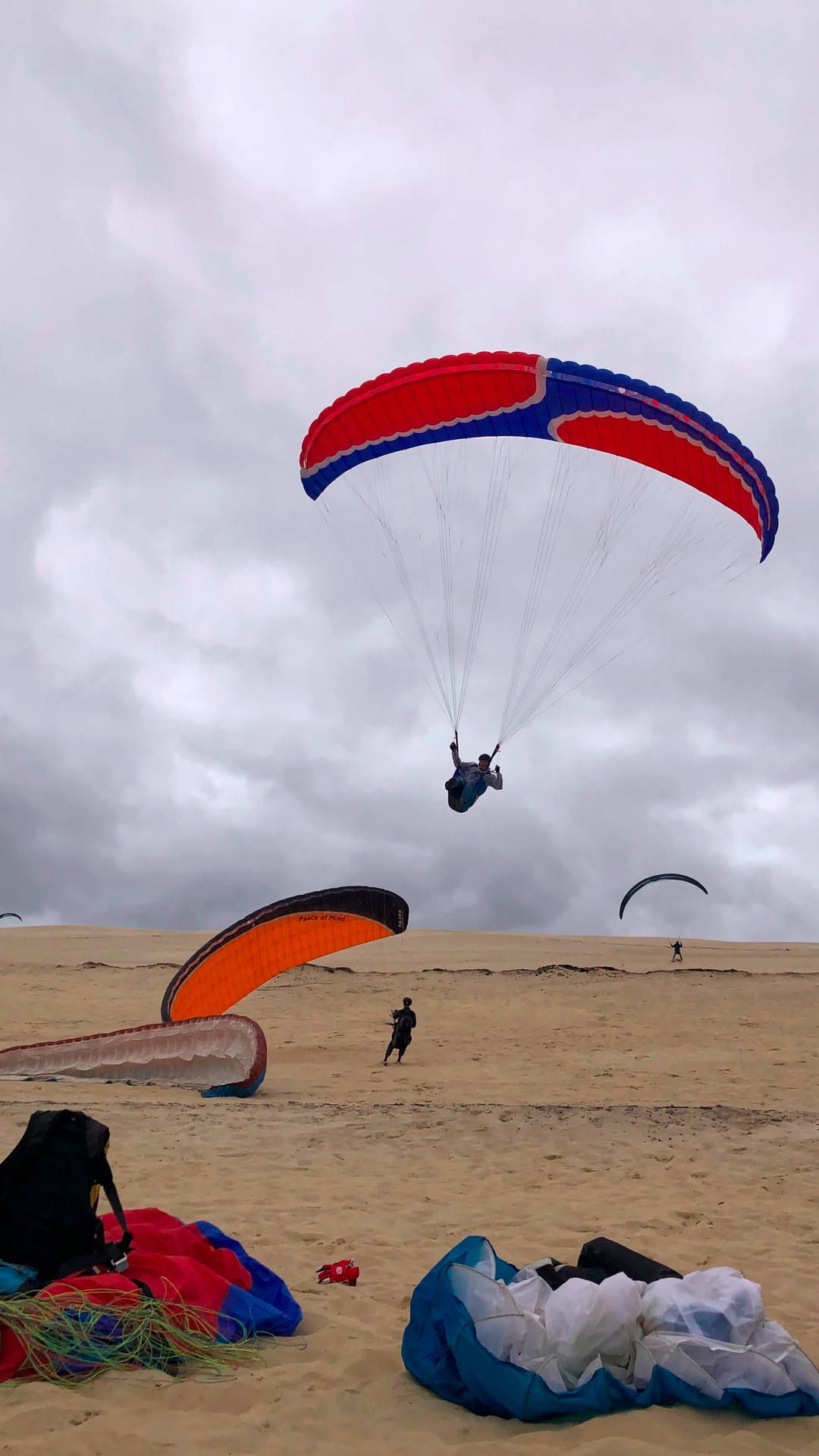Ein Pilot fliegt, ein anderer zieht gerade auf und ein dritter wartet mit aufgezogenem Gleitschirm auf eine Böe um gleich leichtfüssig abzuheben.