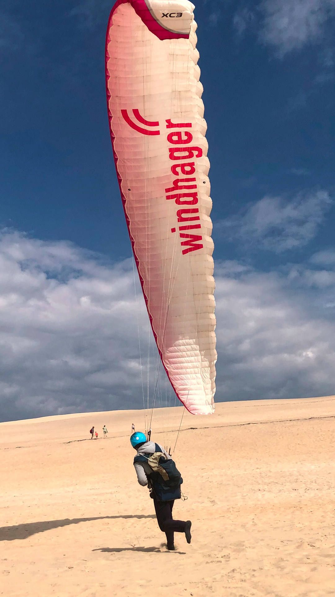 Ein Gleitschirmpilot kitet mit seinem Gleitschirm gekonnt und leichtfüssig über den Sand die Düne hoch.