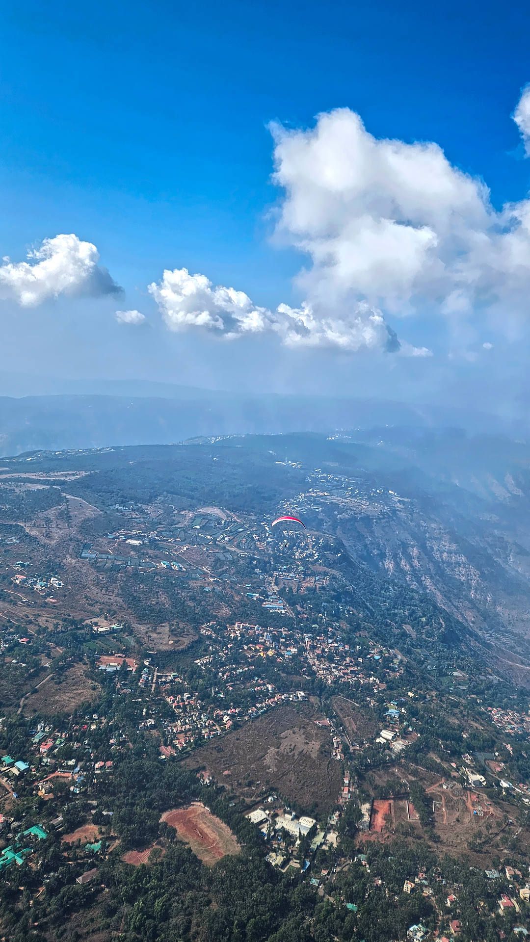 Flugaufnahme: Streckenflug in Richtung Mahableshwar. Ein roter Gleitschirm überfliegt Pangari um bei der nächsten Cumulus-Wolke wieder aufzudrehen.