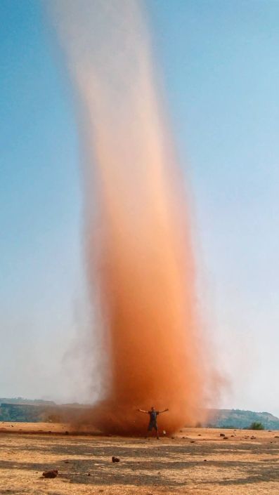 Ein riesiger Dust Devil auf dem Tabeleland von Panchgani. Davor steht ein Mensch mit ausgebreiteten Armen um die Grössenverhältnisse zu verdeutlichen.